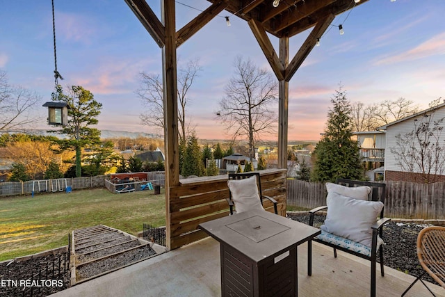 patio terrace at dusk featuring a fenced backyard, a playground, and a lawn