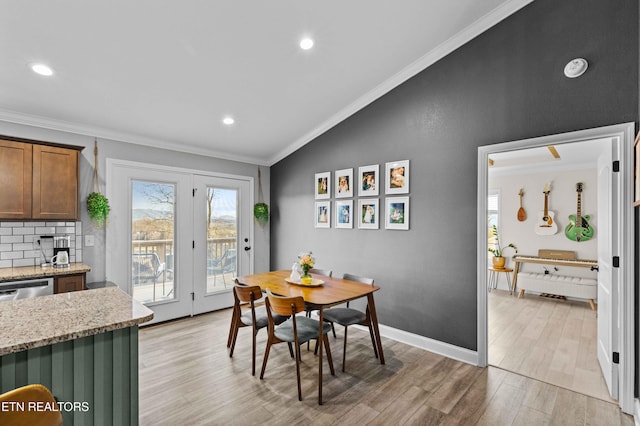 dining room with ornamental molding, lofted ceiling, baseboards, and light wood finished floors