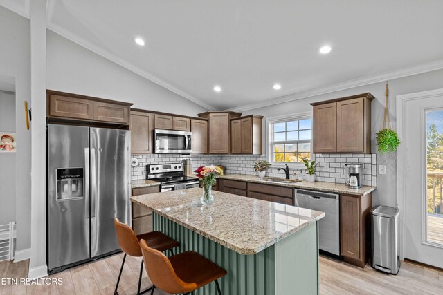 kitchen featuring lofted ceiling, a kitchen island, appliances with stainless steel finishes, light wood-type flooring, and a sink