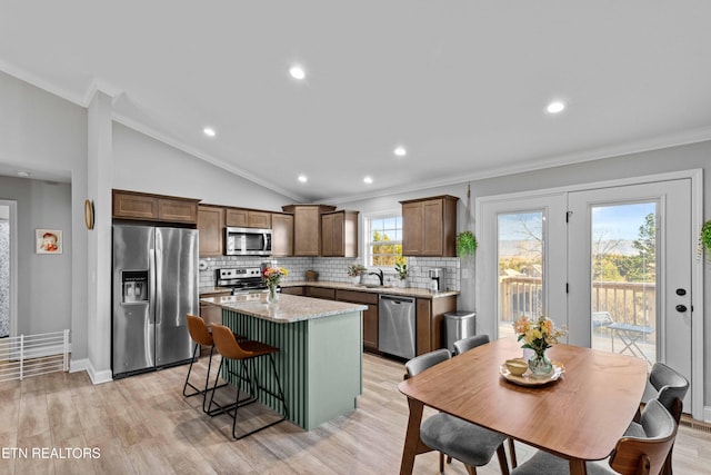 kitchen featuring lofted ceiling, a kitchen island, light wood-style floors, appliances with stainless steel finishes, and crown molding