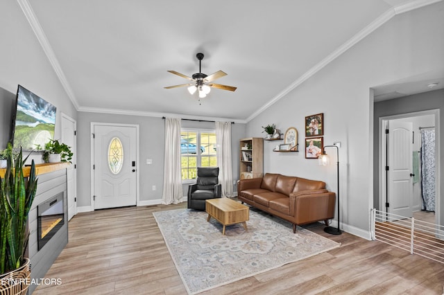 living area featuring crown molding, a glass covered fireplace, vaulted ceiling, and light wood finished floors