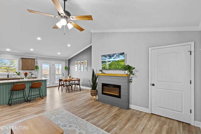 living area with light wood-type flooring, ornamental molding, and a glass covered fireplace