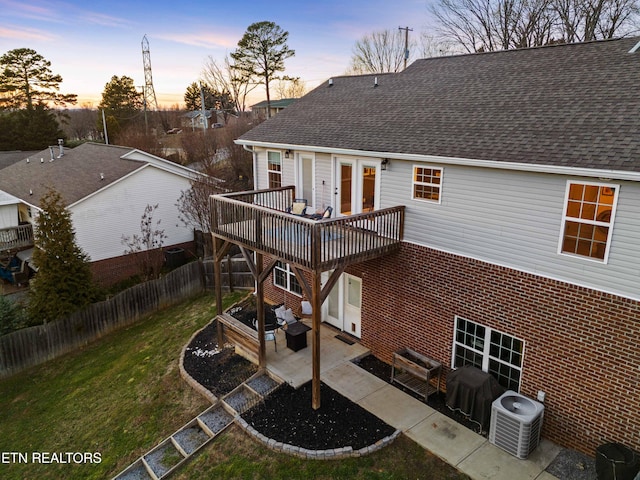 back of property at dusk featuring a patio, cooling unit, a shingled roof, brick siding, and a yard