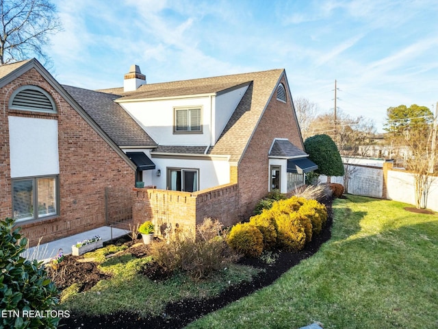 view of side of home with stucco siding, a lawn, fence, a shingled roof, and a chimney