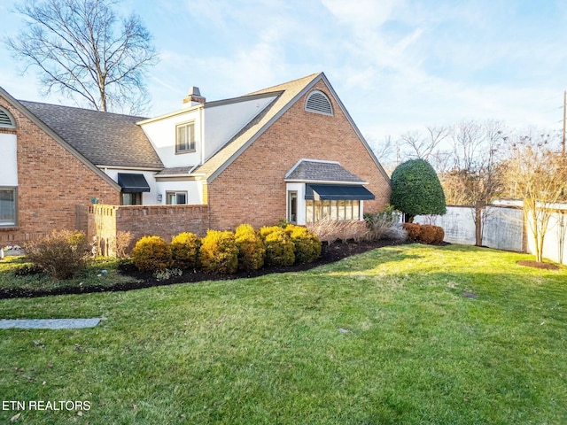 view of property exterior featuring brick siding, fence, roof with shingles, a chimney, and a yard