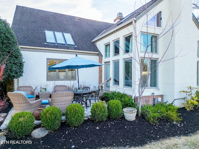 back of house featuring a shingled roof, a patio area, a chimney, and stucco siding