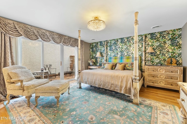 bedroom featuring an inviting chandelier, access to exterior, wood finished floors, and visible vents