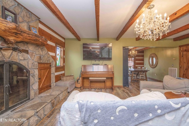 living room featuring visible vents, wood finished floors, beam ceiling, a stone fireplace, and a notable chandelier