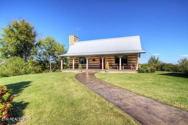 rear view of house with covered porch, a lawn, a chimney, and metal roof