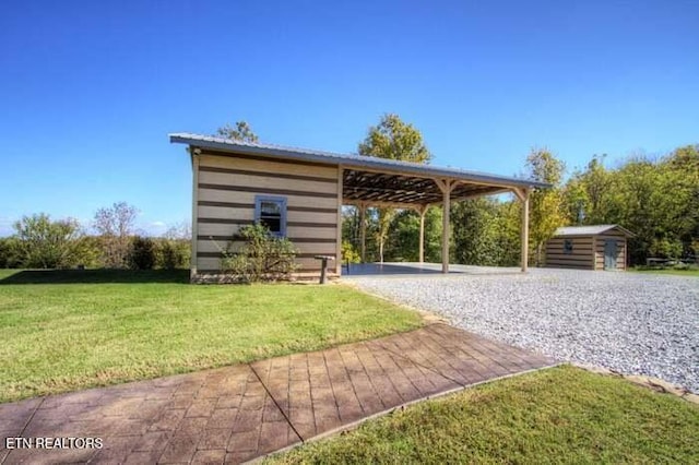 view of community with driveway, a yard, an outdoor structure, a shed, and a carport