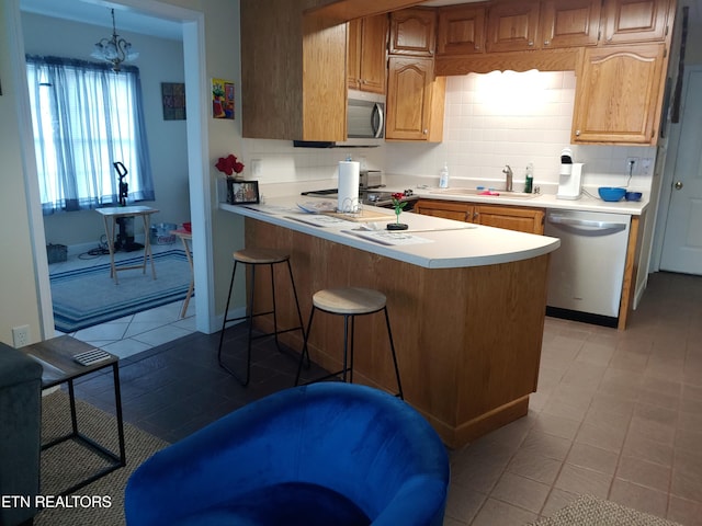 kitchen featuring a sink, a kitchen breakfast bar, light countertops, appliances with stainless steel finishes, and decorative backsplash