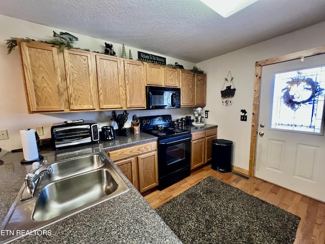 kitchen featuring dark countertops, light wood-style flooring, a sink, a textured ceiling, and black appliances