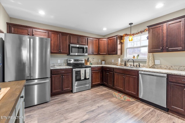 kitchen featuring light wood finished floors, stainless steel appliances, pendant lighting, a sink, and recessed lighting