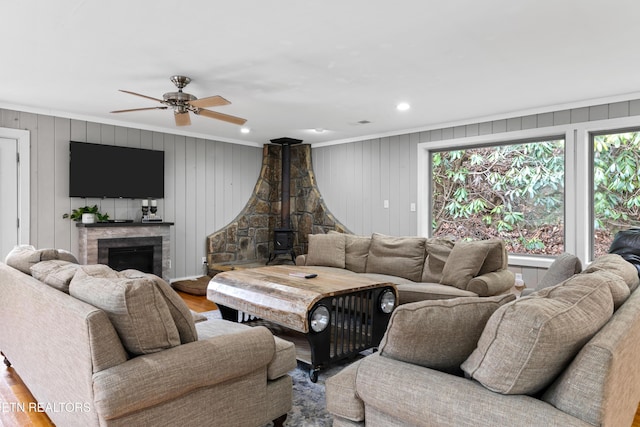 living area with ceiling fan, ornamental molding, wood finished floors, a wood stove, and a fireplace