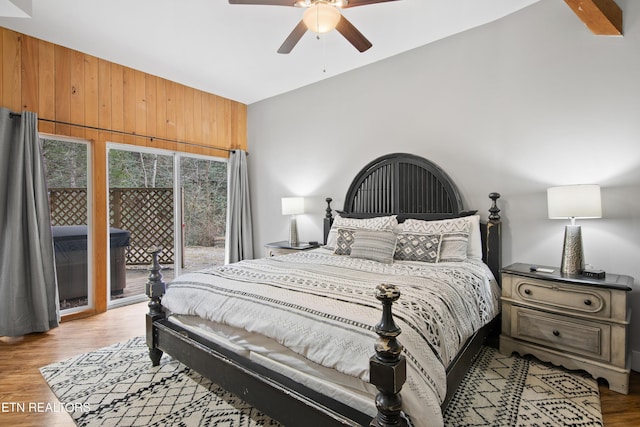 bedroom featuring ceiling fan, wood walls, vaulted ceiling, access to outside, and light wood-type flooring