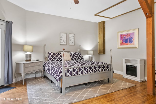 bedroom with baseboards, a ceiling fan, wood finished floors, and a glass covered fireplace