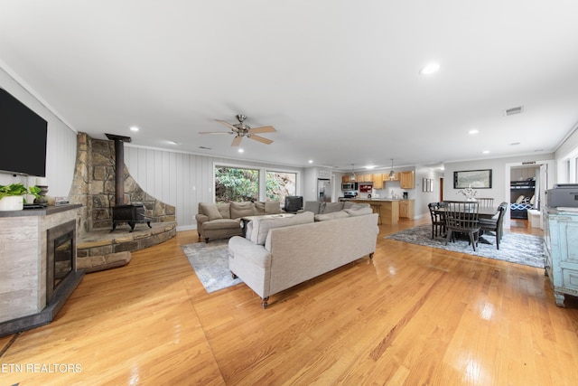 living room featuring light wood-style floors, a wood stove, visible vents, and crown molding