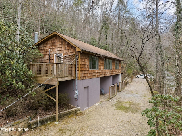 view of home's exterior with driveway, a deck, and a wooded view