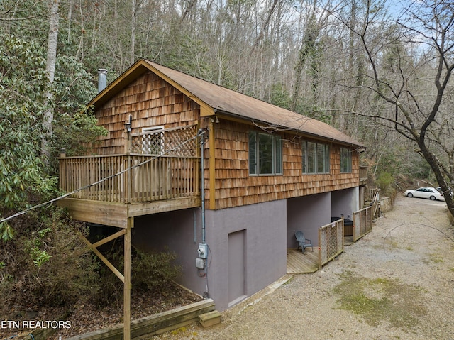 view of side of property featuring a deck, gravel driveway, and a wooded view