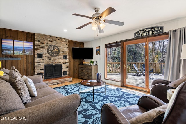 living room featuring ceiling fan, a brick fireplace, wood finished floors, and wooden walls