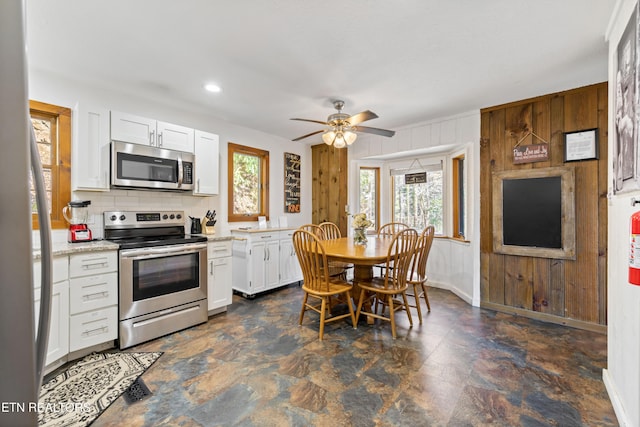 kitchen featuring backsplash, appliances with stainless steel finishes, white cabinetry, wood walls, and baseboards