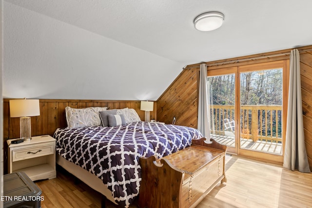 bedroom with access to exterior, light wood-style flooring, wooden walls, and vaulted ceiling