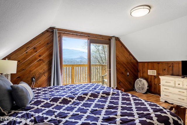 bedroom featuring lofted ceiling, access to outside, light wood-type flooring, and wooden walls