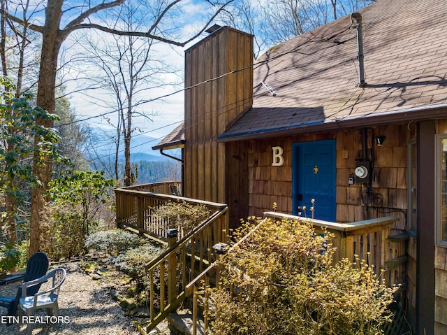 entrance to property featuring a chimney and roof with shingles