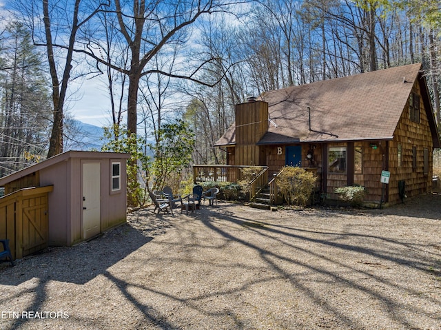 view of side of home featuring a storage shed, a chimney, roof with shingles, an outbuilding, and a wooden deck