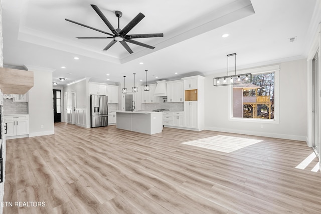 unfurnished living room with light wood finished floors, a raised ceiling, a ceiling fan, and ornamental molding