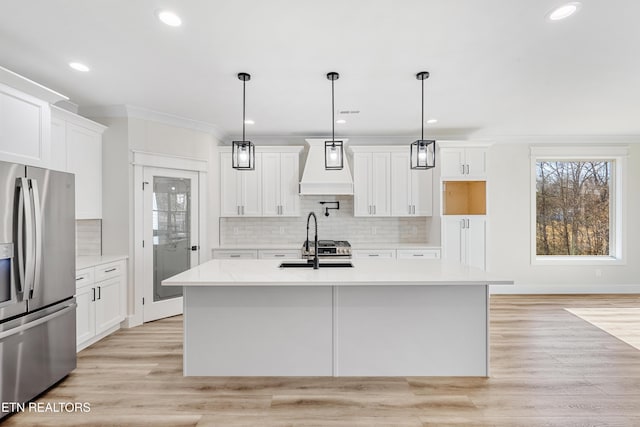 kitchen featuring premium range hood, light wood-style flooring, a kitchen island with sink, a sink, and stainless steel refrigerator with ice dispenser