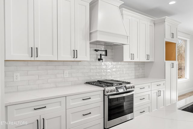 kitchen with light stone counters, premium range hood, decorative backsplash, stainless steel gas range oven, and white cabinetry