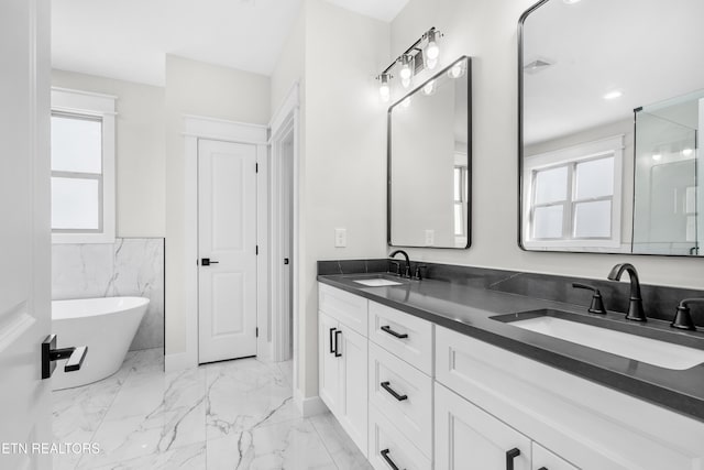 full bath featuring a sink, a freestanding tub, marble finish floor, and double vanity