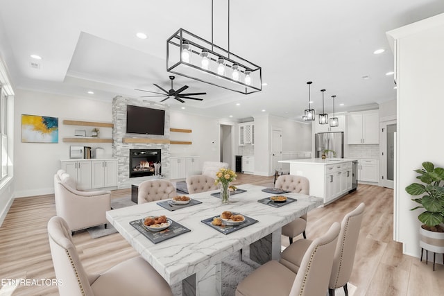 dining area featuring light wood finished floors, crown molding, a large fireplace, and a tray ceiling