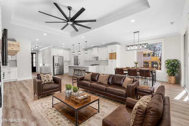 living area with recessed lighting, light wood-style flooring, crown molding, and a raised ceiling