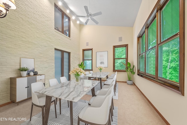 dining area with baseboards, ceiling fan, high vaulted ceiling, and light colored carpet