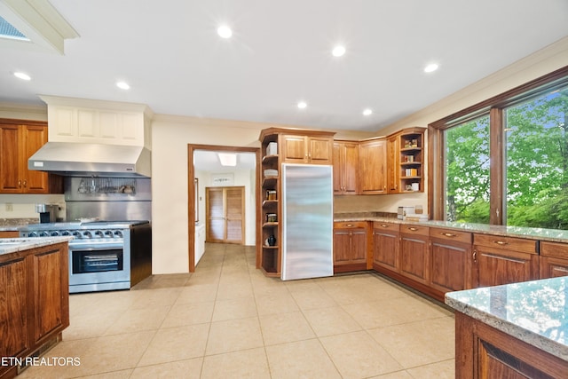 kitchen featuring wall chimney range hood, stainless steel appliances, open shelves, and light stone counters
