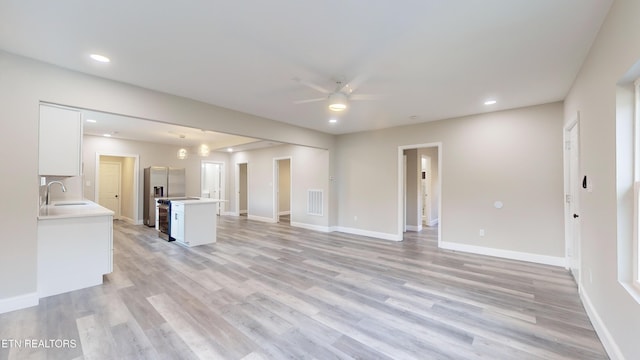 unfurnished living room with visible vents, a sink, light wood-style flooring, and baseboards