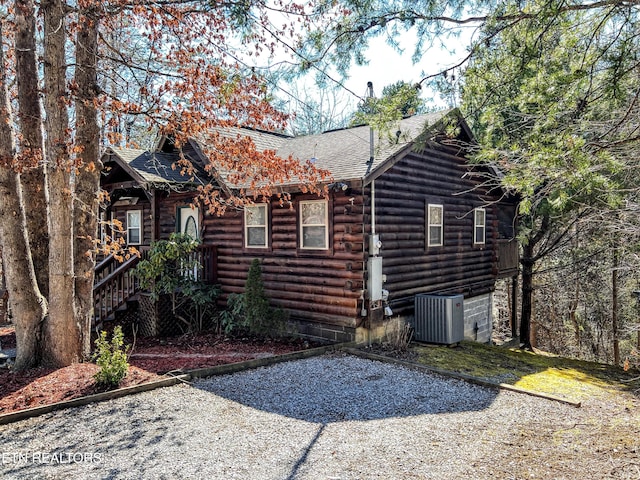 exterior space featuring log exterior, central AC unit, and roof with shingles