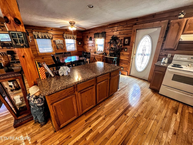 kitchen with light wood-style floors, wood walls, electric range, and a textured ceiling