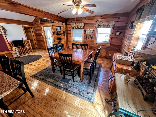 dining area with vaulted ceiling with beams, wood-type flooring, wood walls, and ceiling fan