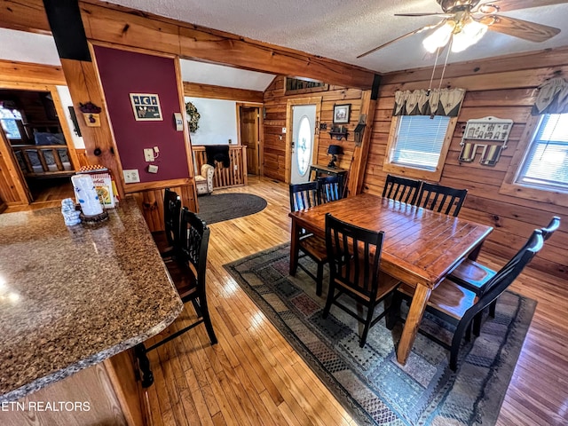 dining area with a textured ceiling, ceiling fan, lofted ceiling with beams, hardwood / wood-style flooring, and wooden walls