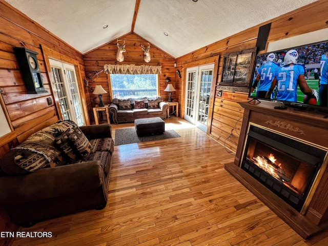 living room featuring lofted ceiling, a textured ceiling, wood-type flooring, and a glass covered fireplace