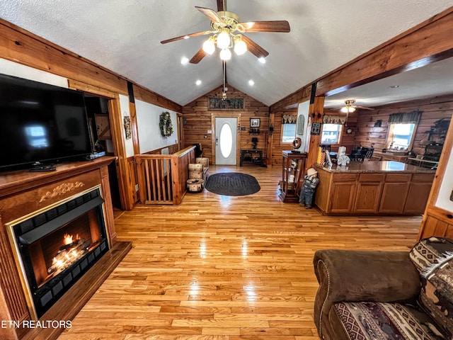 living room featuring a wealth of natural light, ceiling fan, wooden walls, and light wood finished floors