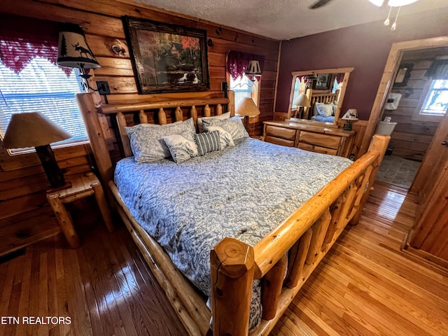 bedroom with wood-type flooring, wooden walls, and a textured ceiling