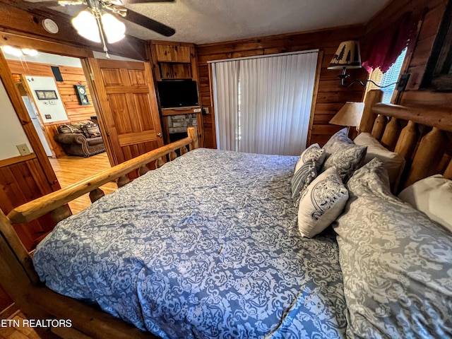 bedroom with a textured ceiling, ceiling fan, wooden walls, and wood finished floors