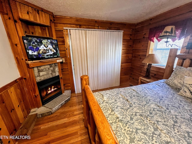 bedroom featuring wooden walls, a fireplace, a textured ceiling, and wood finished floors