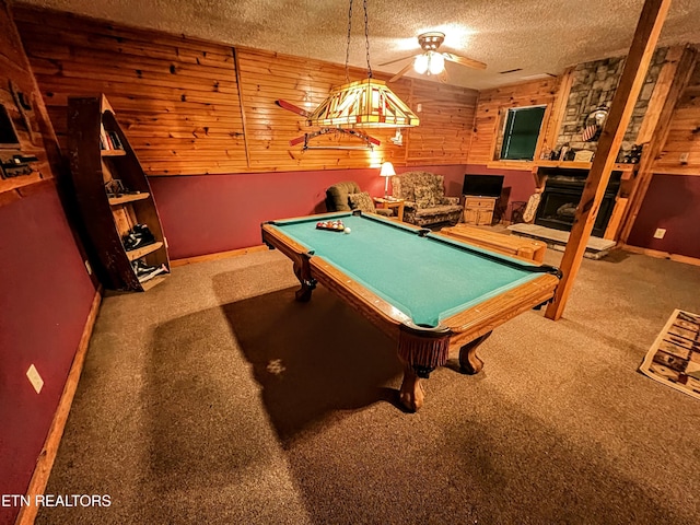 game room featuring carpet floors, wooden walls, a textured ceiling, and a stone fireplace