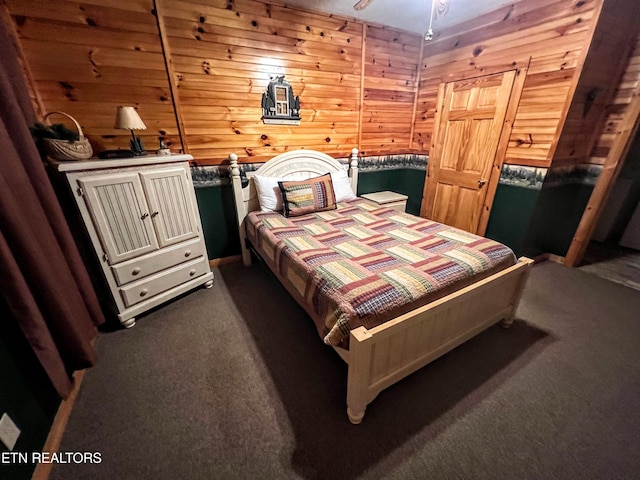 bedroom featuring wooden walls and dark colored carpet