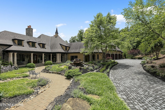 back of house featuring a garage, a chimney, and decorative driveway